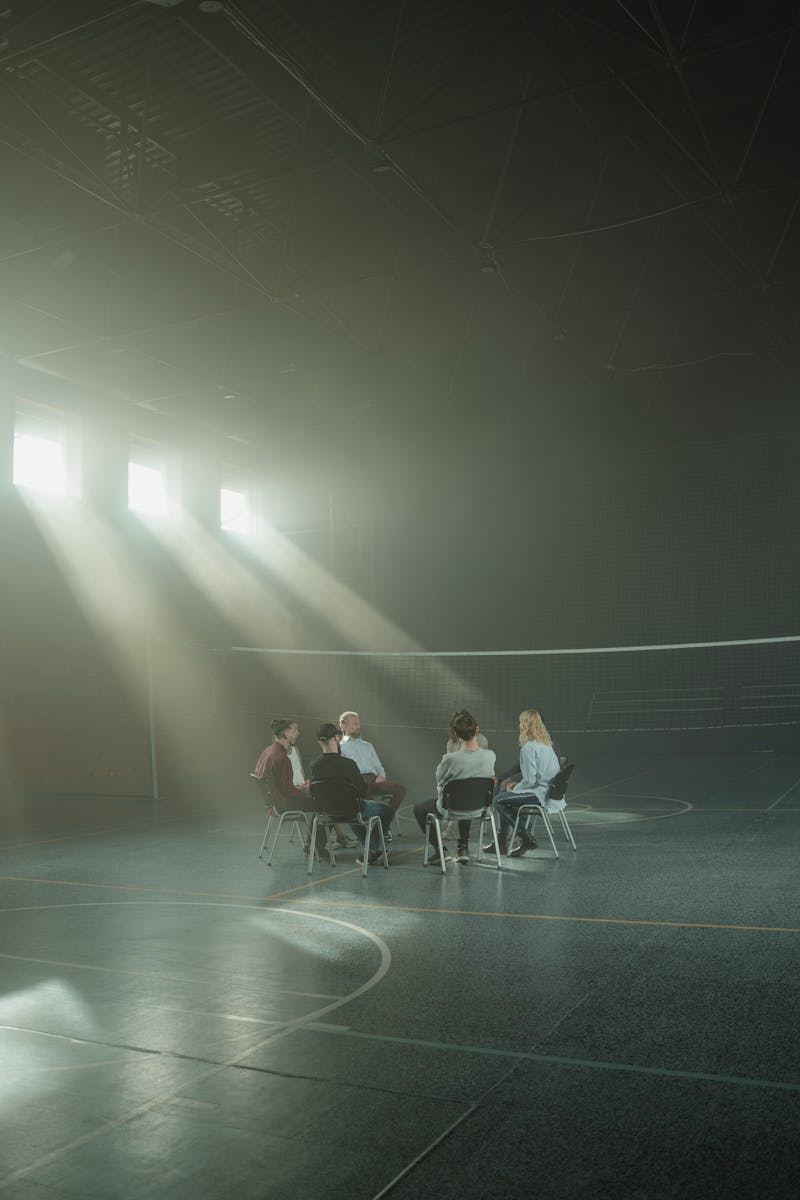 A small group of people engaging in a therapy session in a spacious, dimly lit indoor hall.